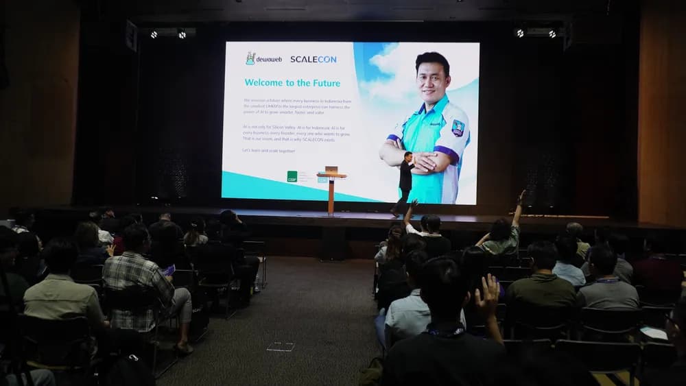 A speaker on the SCALECON Jakarta 2025 main stage as attendees raise their hands