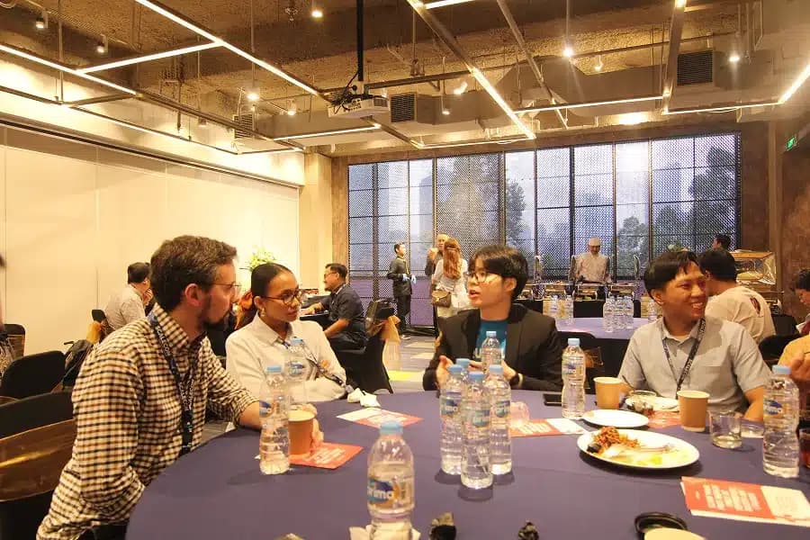 Attendees eating and talking at a long table by the windows at a previous SCALECON